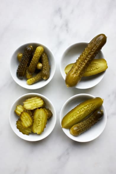 Vier Keramikschalen mit verschiedenen Gewürzgurkensorten: Cornichons, Dillstange, süße Scheiben und Kosher Dill