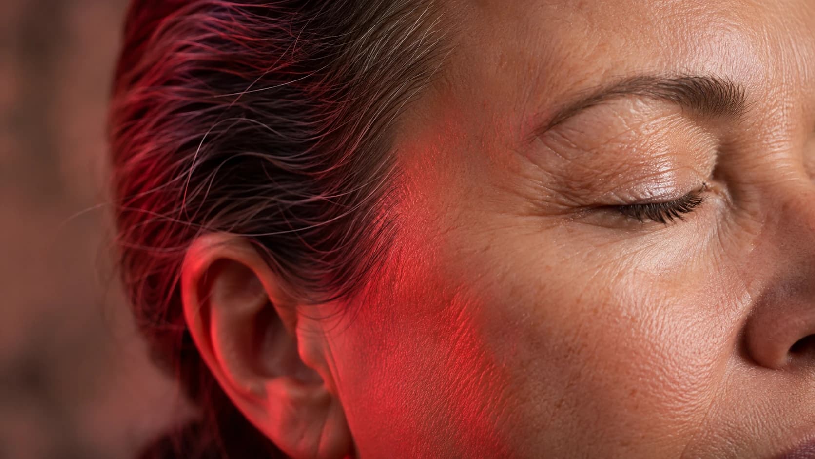 Close-up of mature facial skin lit by red therapy light, showing natural texture and fine lines
