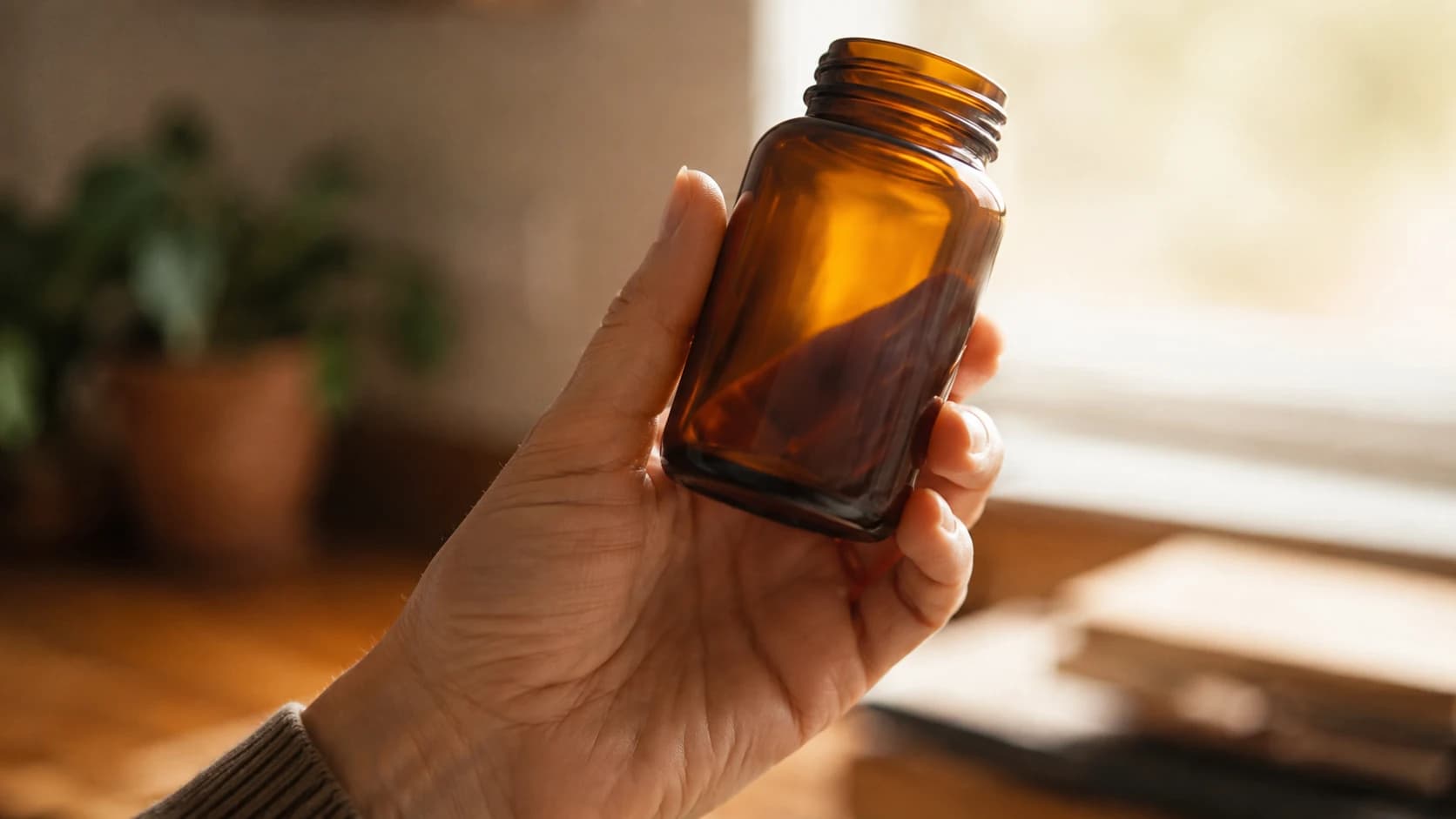 A hand holding a plain unlabelled bottle up to the light to read the back