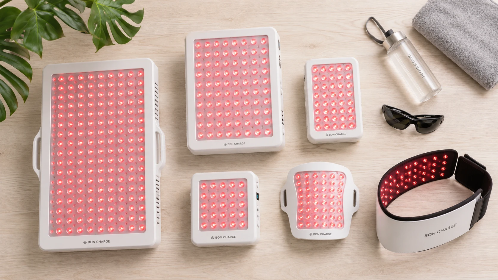 Flatlay of six red light therapy devices for muscle recovery, including panels of various sizes and a wearable wrap on a light wood surface